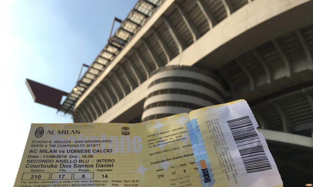 ingresso amarelo para entrar no estádio do Milan, o San Siro. Ao fundo da imagem está o próprio estádio