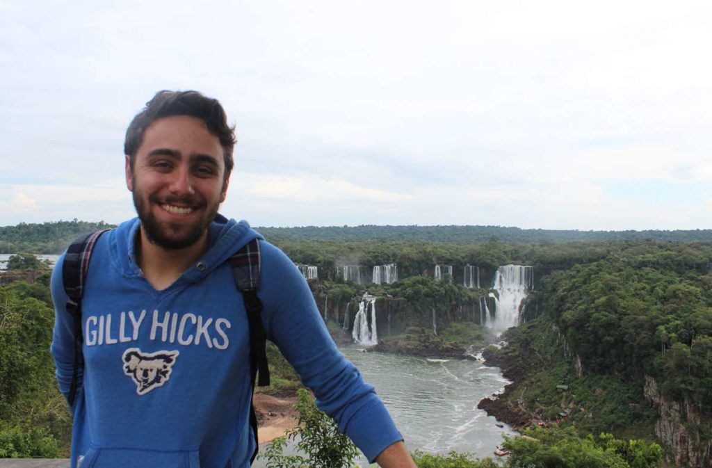 homem de moletom azul no primeiro plano e as cataratas do iguacu em segundo