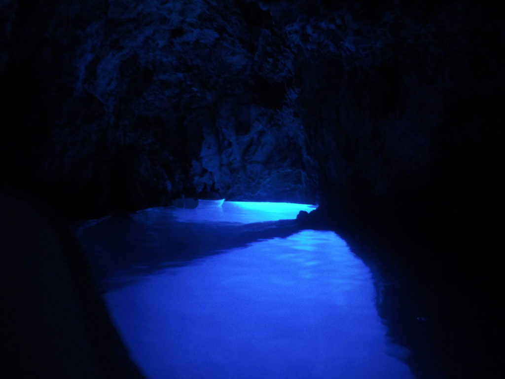 Dentro da blue cave, a cova azul em uma ilha croata. à frente está um pequeno barco e ao redor uma luz forte azul compõe o resto do cenário