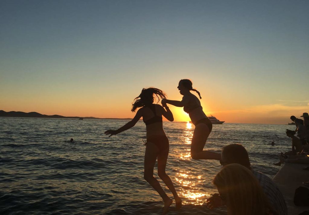 meninas pulam no mar de Zadar ao pôr do sol