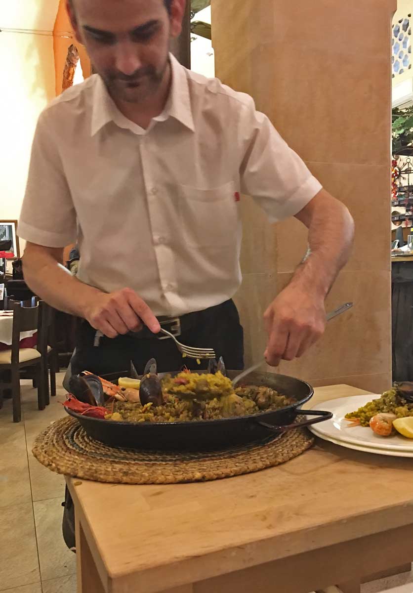 garcom servindo paella em mesa de restaurante em pollenca