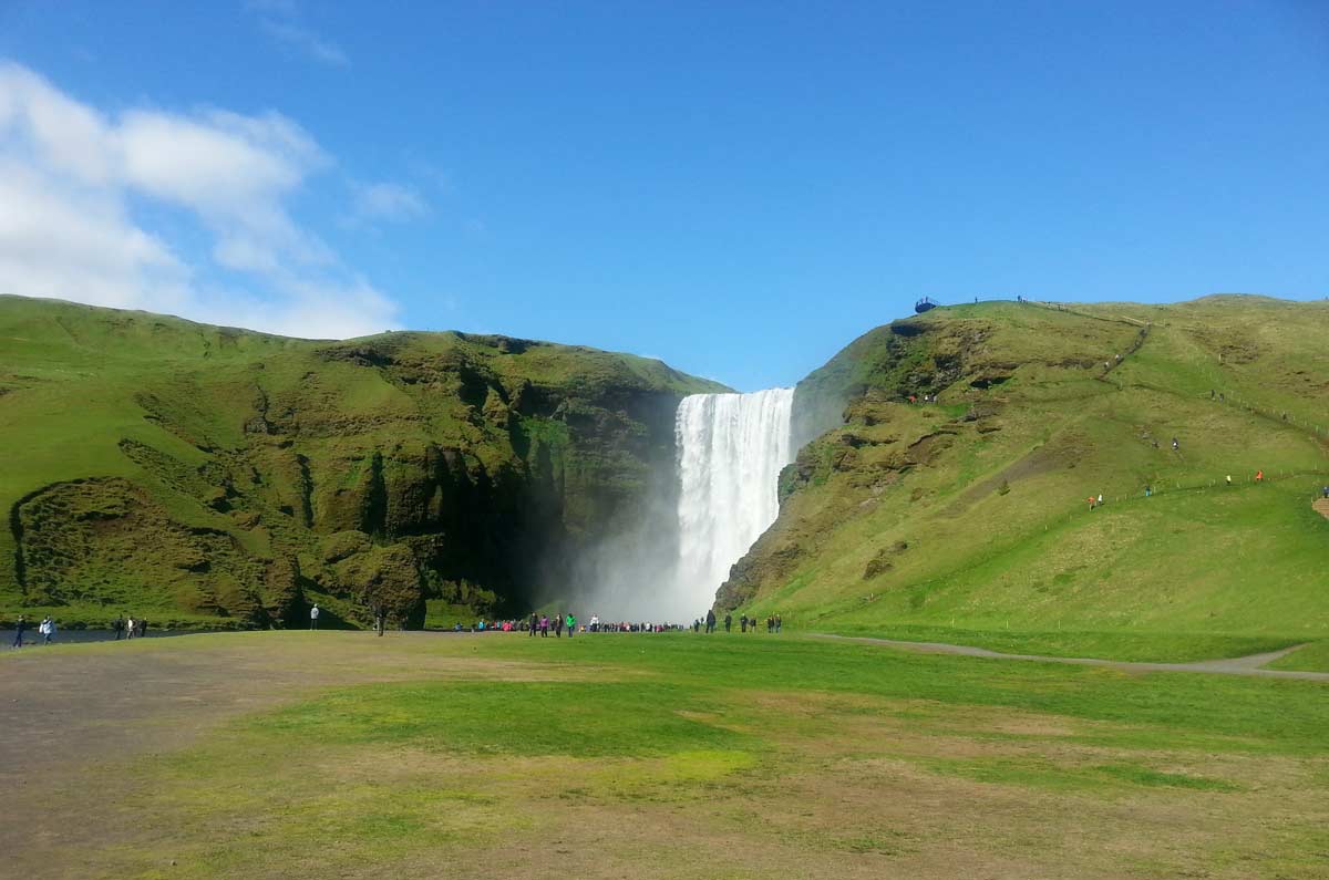 skogafoss, uma das cachoeiras mais bonitas da ilândia ao fundo da imagem, cercada de verde