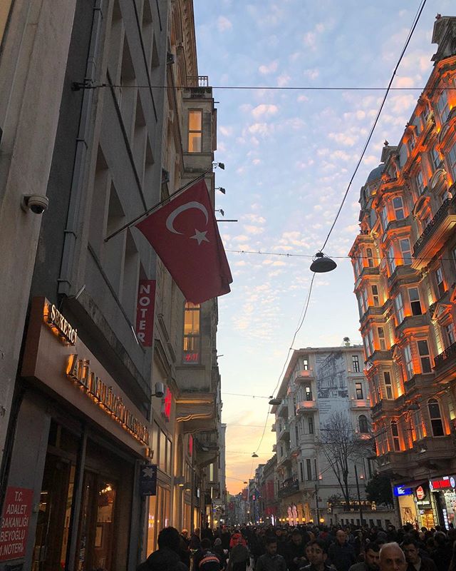 rua de compras de istambul. na foto, bandeira da turquia aparece pendurada em um prédio e o céu está azul