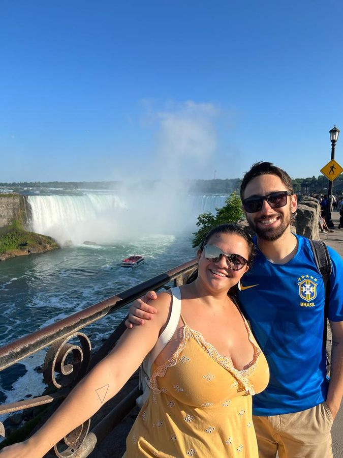 casal posa em frente as cataratas do niágara em dia ensolarado no Canadá