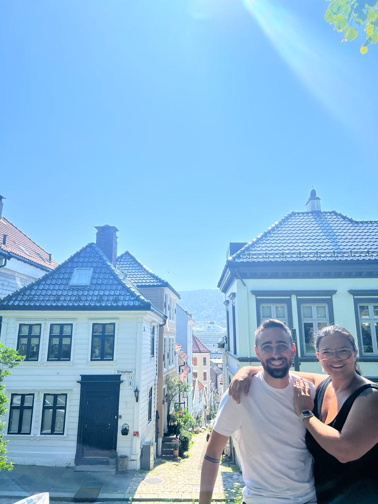 casal posa em frente a uma rua com casas norueguesas tradicionais